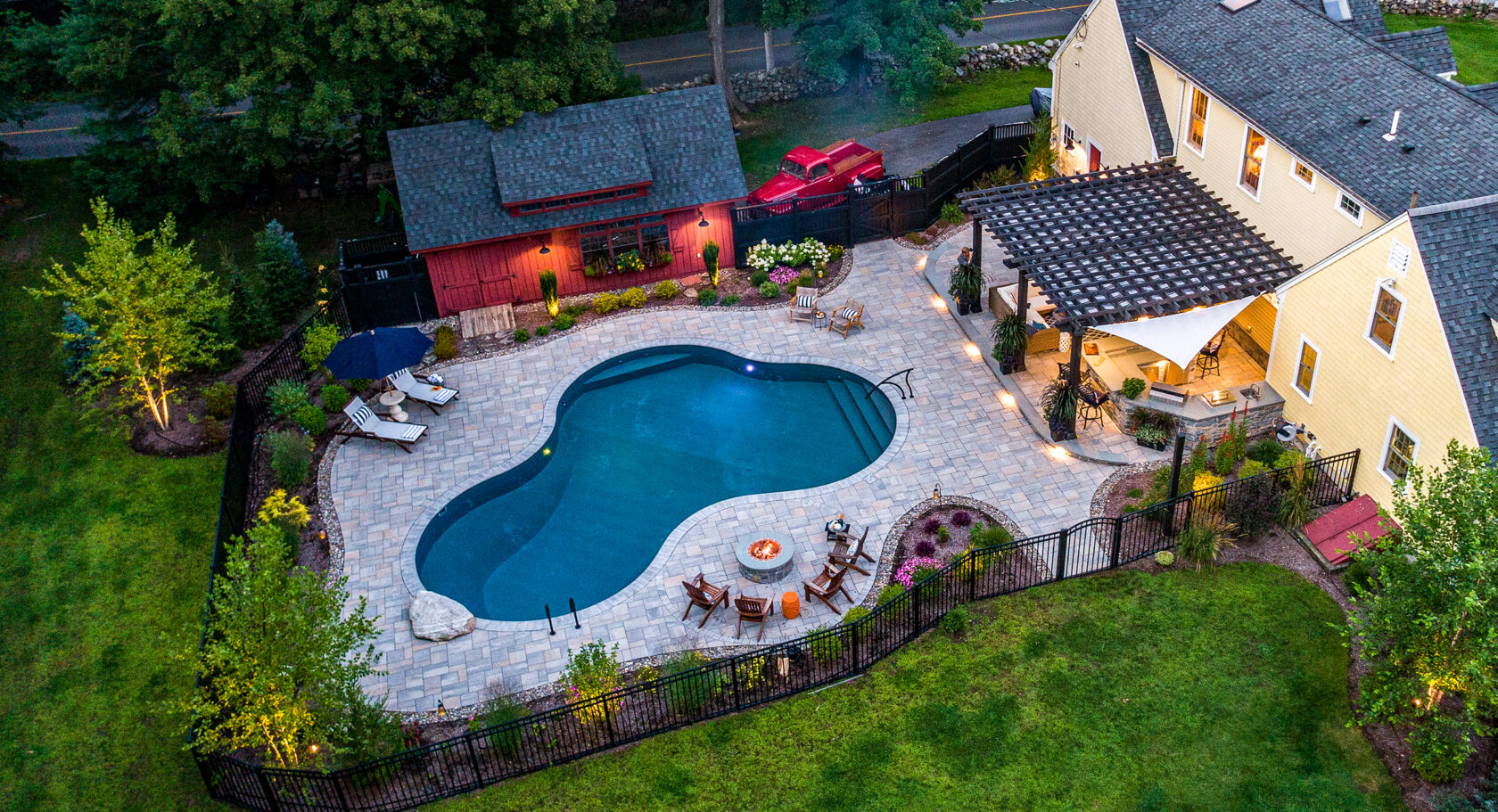 Drone view of pool deck, fire pit, and outdoor kitchen at Dex by Terra's residential landscape design project in Stow, MA.