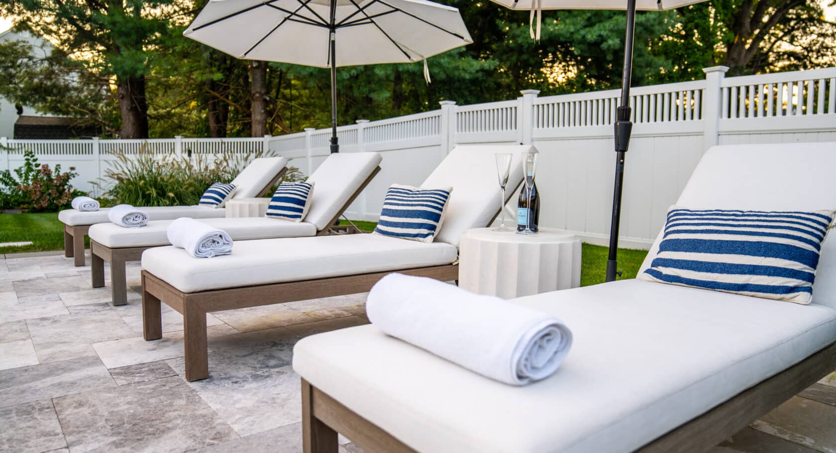 Sun chairs on stone poolside patio in Andover, Massachusetts. Dex by Terra Landscape Design and Build project.