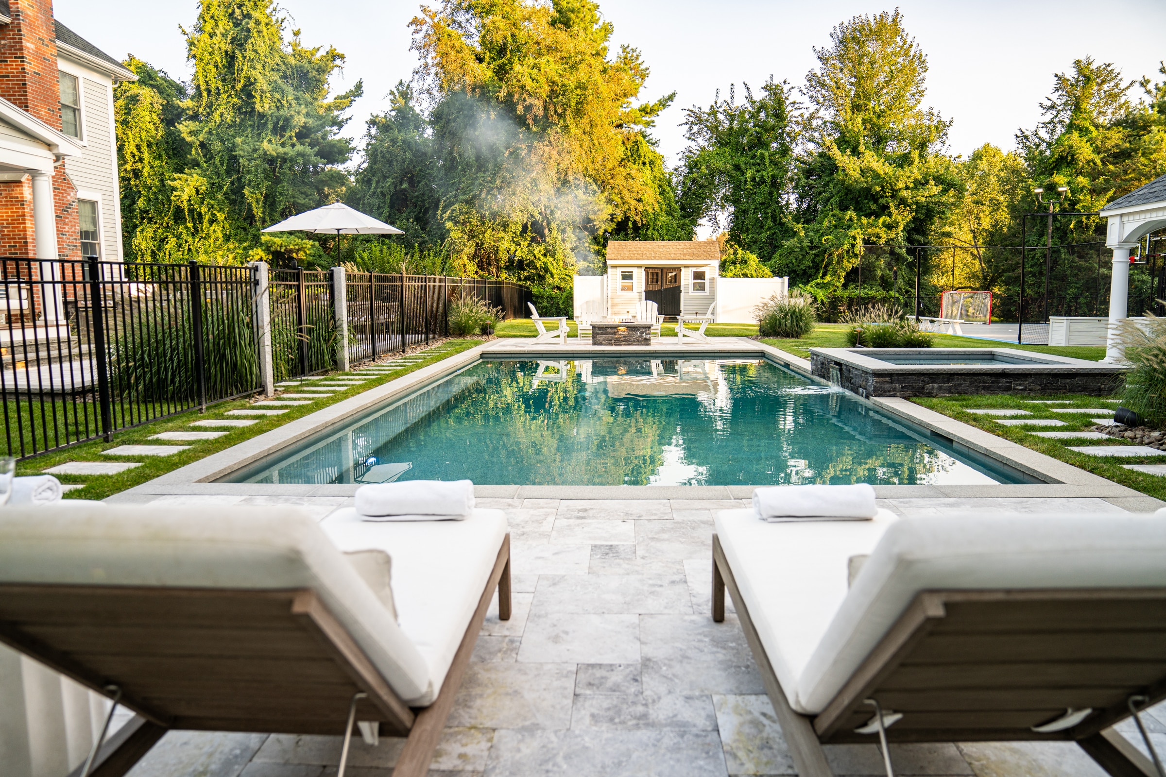 Stone paver pool deck with sun chairs. Dex by Terra Landscape design / build project in Andover, Massachusetts.