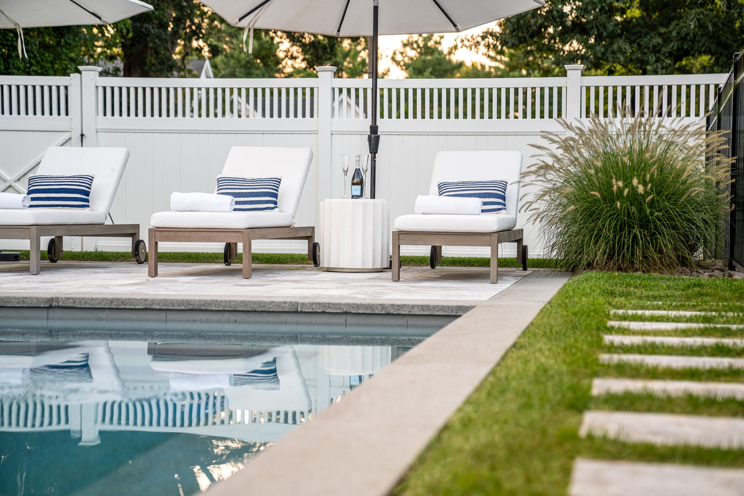 Poolside turf, paver walkway, and patio with sun chairs. Dex by Terra Landscape design / build project in Andover, Massachusetts.