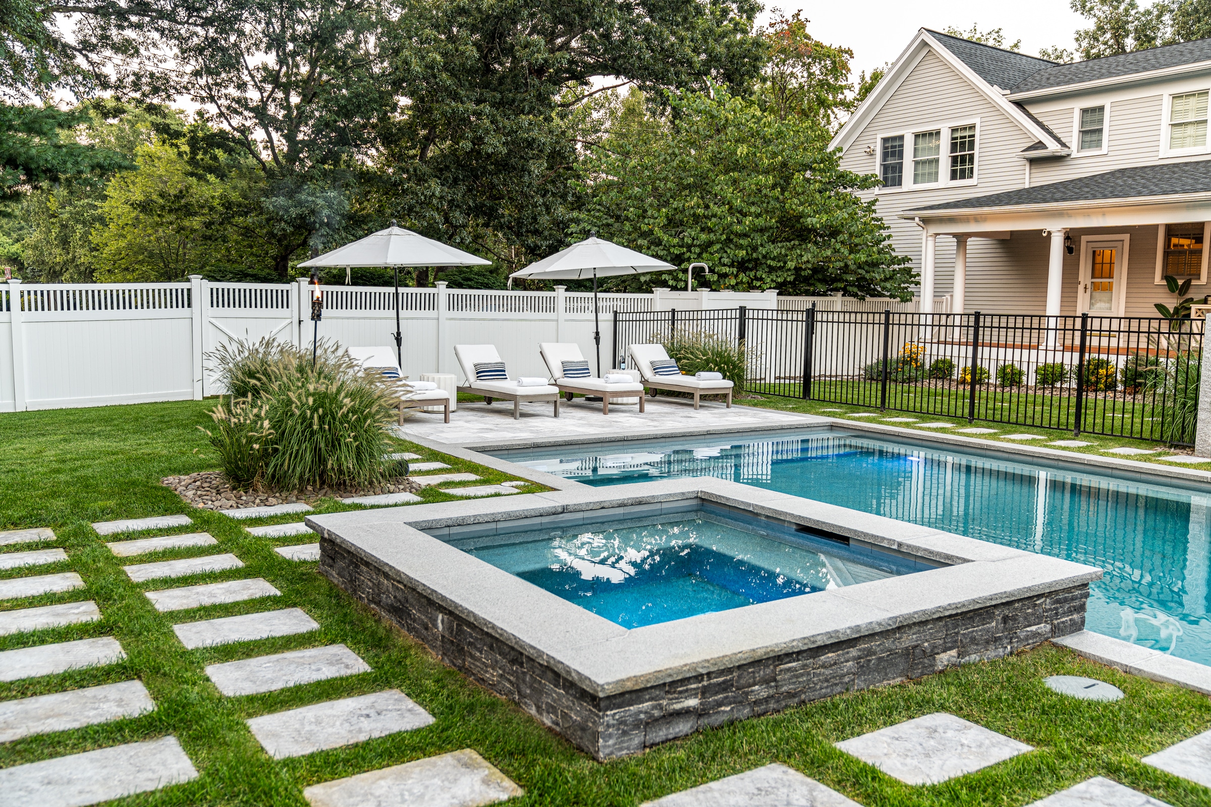 Poolside spa with stone veneer and granite cap in Andover, Massachusetts. Masonry designed and built by Dex by Terra.