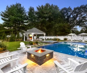 Poolside patio with a fire pit and landscape lighting. Dex by Terra landscape design/build project in Andover, Massachusetts.