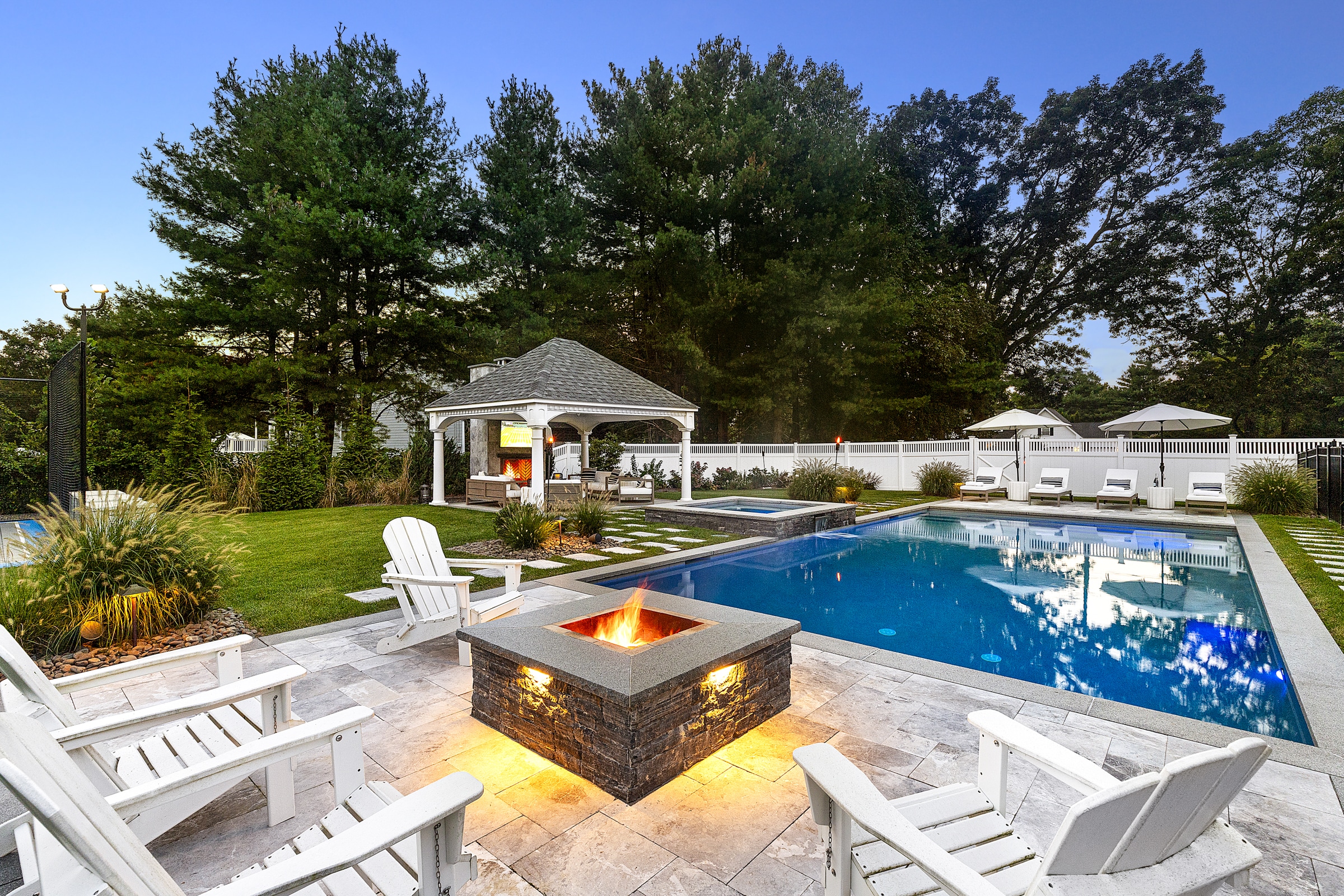 Poolside patio with a fire pit and landscape lighting. Dex by Terra landscape design/build project in Andover, Massachusetts.