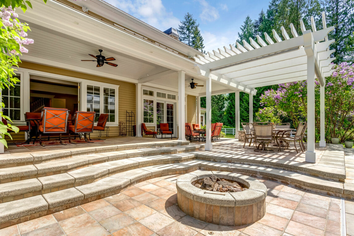 An outdoor structure in Massachusetts with a spacious covered patio, elegant white pergola, and a built-in firepit for relaxation.